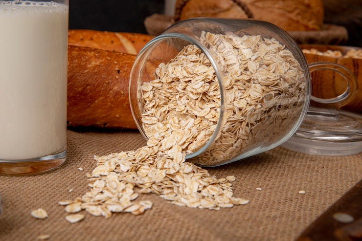 Foto gratuito vista laterale di fiocchi d'avena che si rovesciano dal barattolo sparso con bicchiere di latte sulla superficie della tela di sacco
