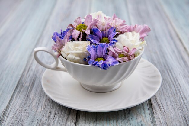 Vista laterale di fiori in tazza sul piattino su sfondo di legno