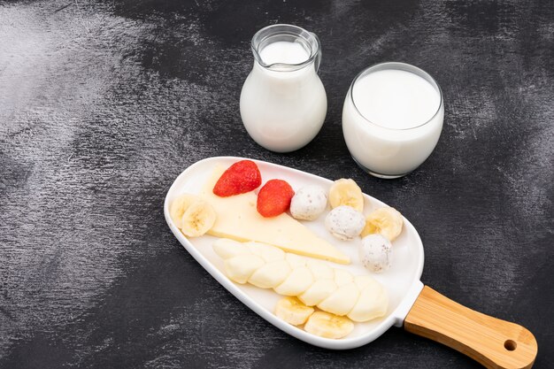 Vista laterale di formaggio con i frutti e il cetriolo di latte sull'orizzontale di superficie del nero