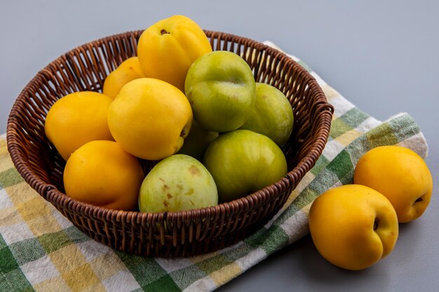 Vista laterale di frutti come pluots verdi e nectacots nel cesto su tela a quadri e su sfondo grigio