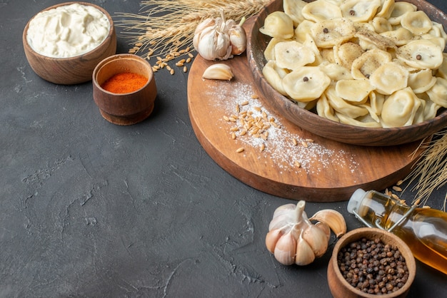 Vista laterale di gnocchi fatti in casa in una ciotola marrone su un tagliere di legno picchi peppers garlics bottiglia di olio caduta sul tavolo scuro con spazio libero