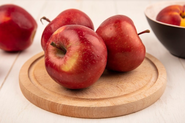 Vista laterale di gustose mele rosse su una tavola da cucina in legno su una superficie di legno bianca