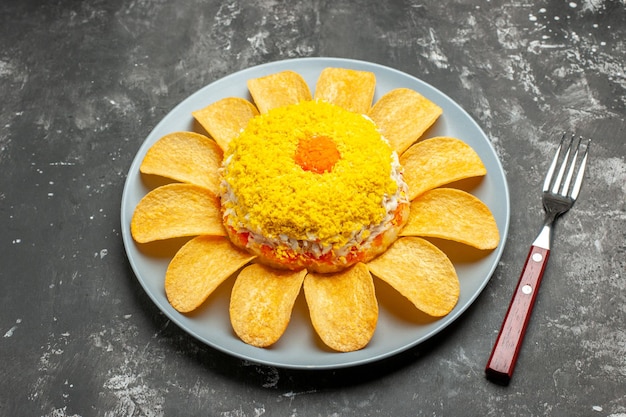 Vista laterale di insalata con patatine intorno sul piatto su sfondo grigio scuro