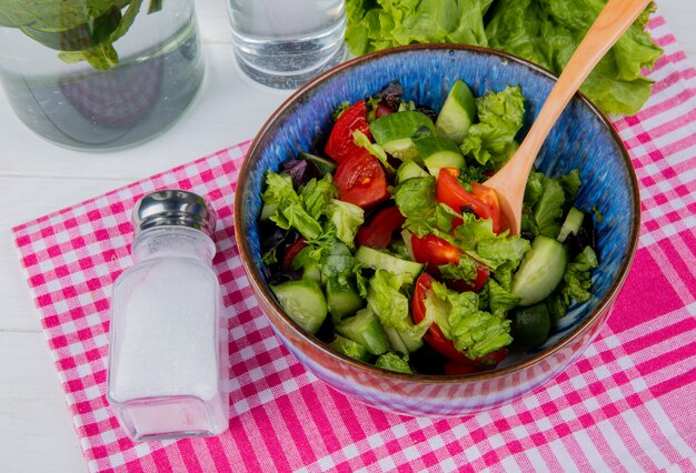 Vista laterale di insalata e sale di verdure sul panno del plaid con acqua della disintossicazione e lattuga sulla tavola di legno