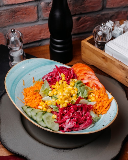 Vista laterale di insalata fresca con i pomodori e il mais tagliati dei cetrioli della carota di cavolo in un piatto