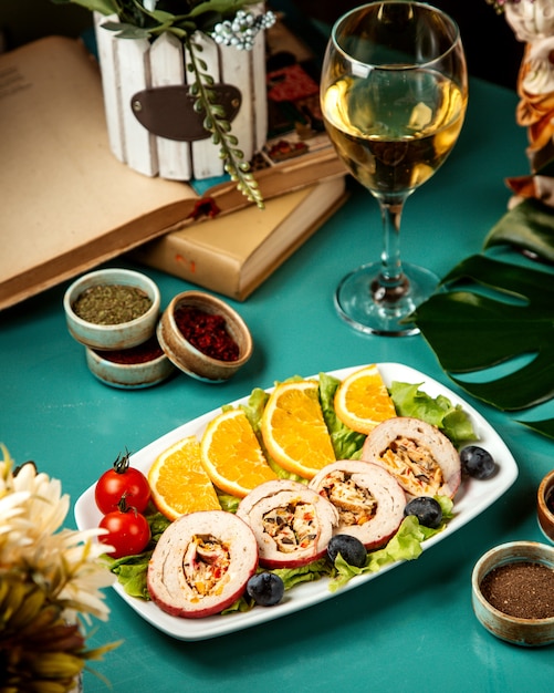 Vista laterale di involtini di pollo ripieni con verdure ed erbe servita con fettine di arancia e pomodorini sul piatto