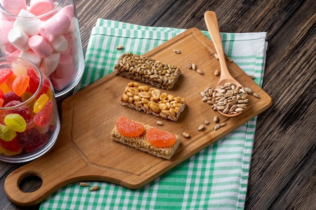 Vista laterale di kozinaki dolce di semi di girasole sesamo e arachidi su una tavola di legno e con caramelle marmellata in barattolo di vetro su rustico