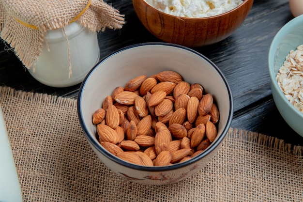 vista laterale di mandorle in ciotola su crema di fiocchi di avena fiocchi di ricotta crema su legno