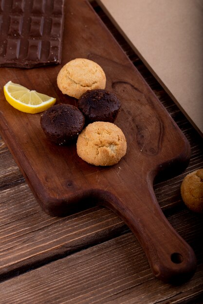 Vista laterale di muffin con fetta di limone e cioccolato fondente su un tagliere di legno