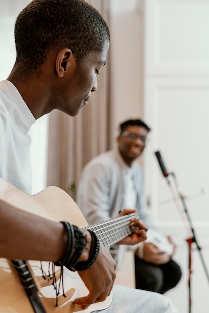 Vista laterale di musicisti maschi a casa a suonare la chitarra