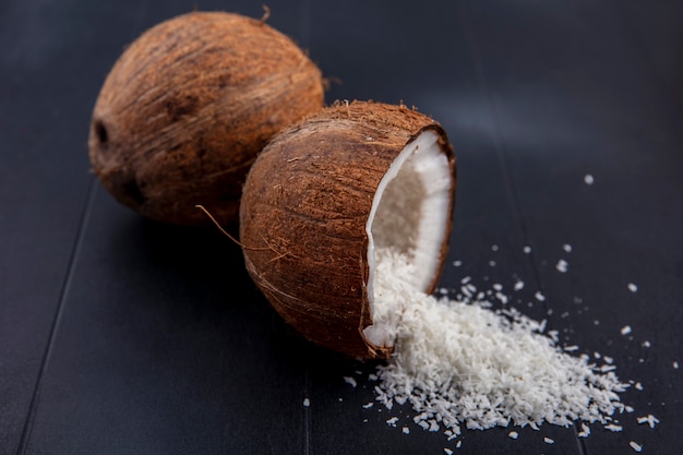 Vista laterale di noci di cocco fresche e marroni con polvere di cocco su una superficie nera