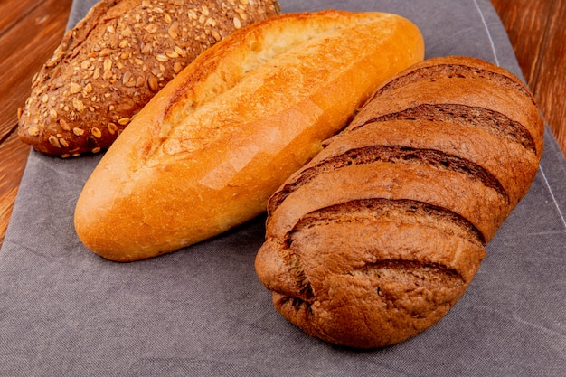 vista laterale di pane come vietnamita e nero baguette con semi e pane nero sul panno grigio e tavolo in legno