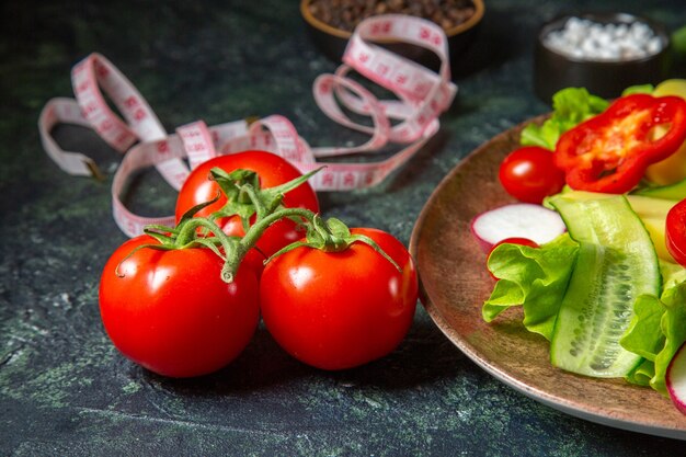 Vista laterale di patate fresche tagliate pelate con peperone rosso ravanelli pomodori verdi in una piastra marrone e metri di spezie su verde nero mescolare i colori dello sfondo