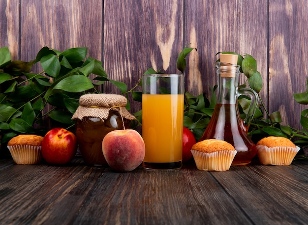 vista laterale di pesche fresche mature con marmellata di pesche muffin in un barattolo di vetro e succo di pesca in un bicchiere sul tavolo di legno rustico