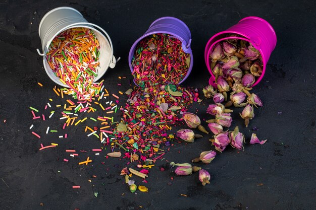 Vista laterale di petali di fiori secchi di tè rosa e spruzzi colorati sparsi da piccoli secchi sul nero