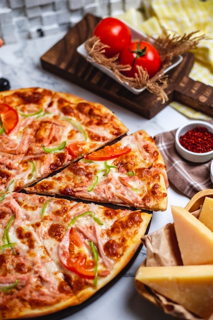 Vista laterale di pizza con i pomodori ed il formaggio verdi del peperoncino del prosciutto sulla tavola