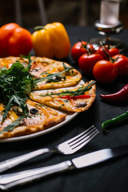 Vista laterale di pizza italiana affettata con i peperoni variopinti funghi rucola e formaggio delle olive nere su un piatto di legno