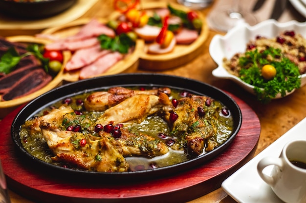 Vista laterale di pollo in umido con verdure a cipolla e melograno in un piatto di argilla