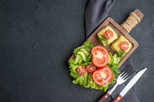 Vista laterale di pomodori freschi tagliati e cetrioli formaggio su tavola di legno sul lato sinistro sulla superficie nera