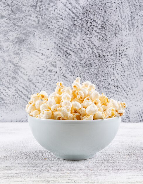 Vista laterale di popcorn in ciotola sul verticale di legno bianco della tavola