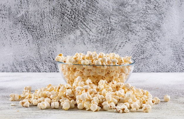 Vista laterale di popcorn in ciotola sulla tavola di legno bianca con l'orizzontale bianco