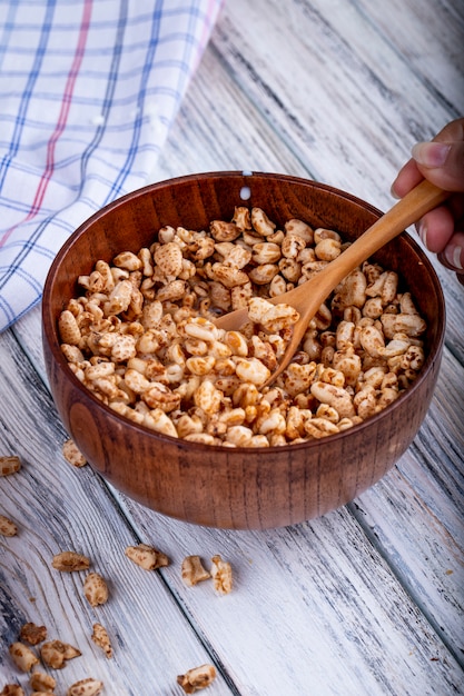 Vista laterale di riso dolce soffiato in una ciotola di legno con un cucchiaio rustico