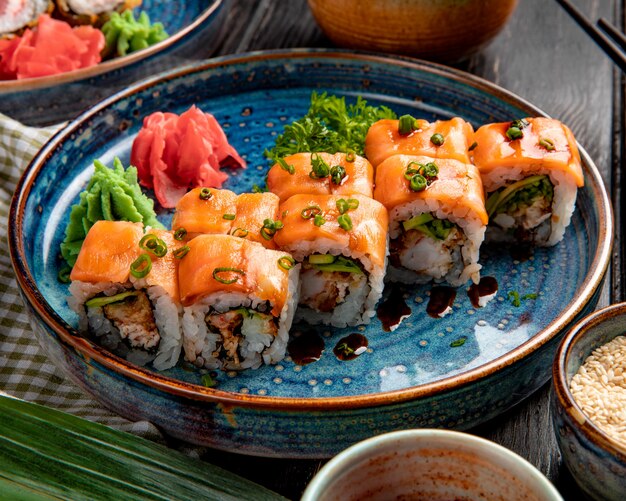 Vista laterale di rotoli di sushi con avocado di anguilla salmone e crema di formaggio su un piatto con zenzero e wasabi