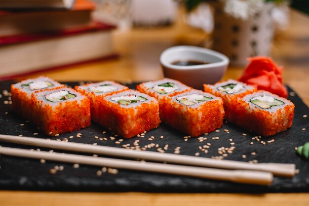Vista laterale di set di sushi rotoli con crema di granchio crema di formaggio e avocado nel caviale di pesce volante con salsa di soia su una lavagna nera