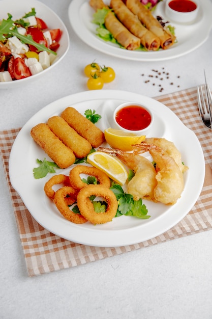 Vista laterale di tempura di calamari e gamberi e bastoncini di formaggio fritto su un piatto bianco