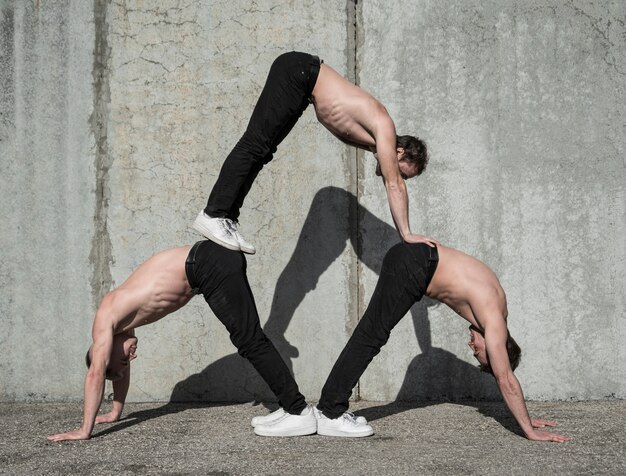 Vista laterale di tre artisti hip-hop senza camicia che praticano la routine di ballo