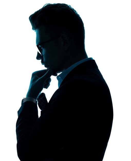 Vista laterale di un bell'uomo di successo in occhiali da vista che indossa in tuta pensieroso e guardando in basso tenendo la mano con l'orologio al polso sul mento e posando su sfondo bianco