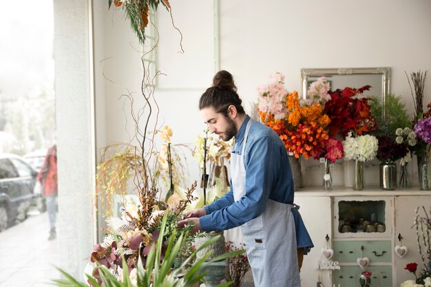 Vista laterale di un fiorista maschio che organizza i fiori nel suo negozio di fiori