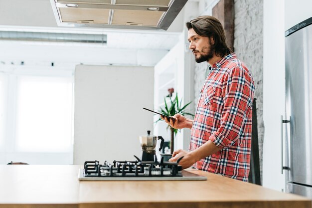 Vista laterale di un giovane in piedi nella cucina tenendo il telefono intelligente