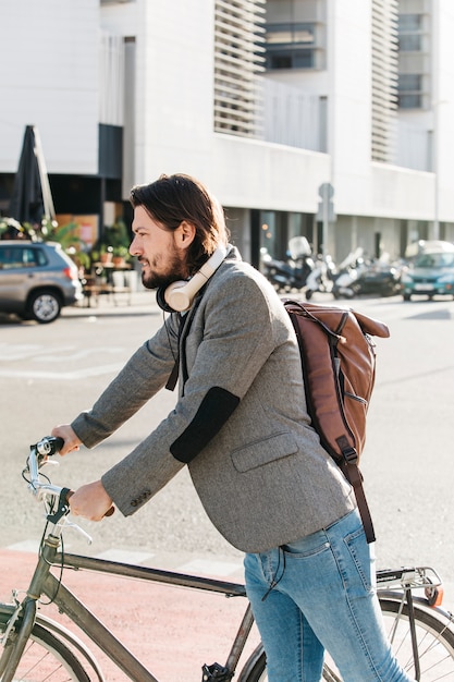 Vista laterale di un uomo che porta zaino in piedi con la sua bicicletta sulla strada