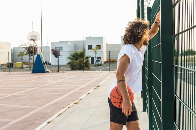 Vista laterale di un uomo con la pallacanestro che osserva attraverso la rete fissa