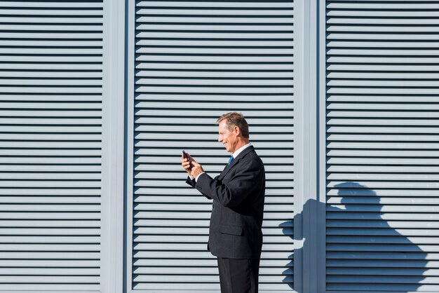 Vista laterale di un uomo d&#39;affari maturo sorridente che utilizza cellulare all&#39;aperto