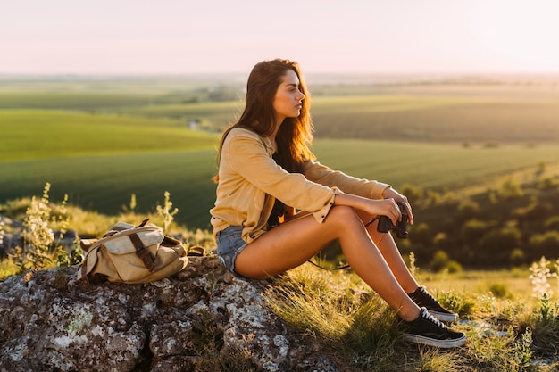 Vista laterale di una bella giovane donna che si siede sulla roccia