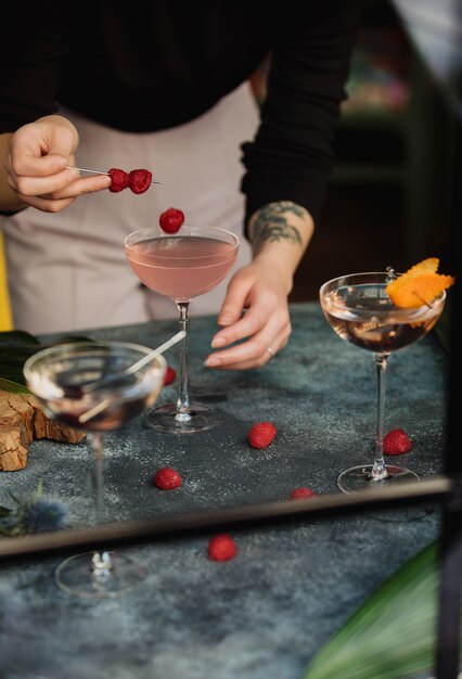 Vista laterale di una donna che decora un cocktail rosa con frutti di bosco