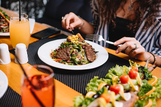 Vista laterale di una donna che mangia insalata di carne di manzo con verdure e semi