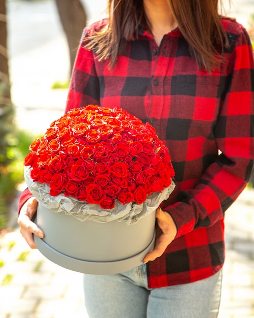 Vista laterale di una donna che tiene una composizione di rose di colore rosso in scatola