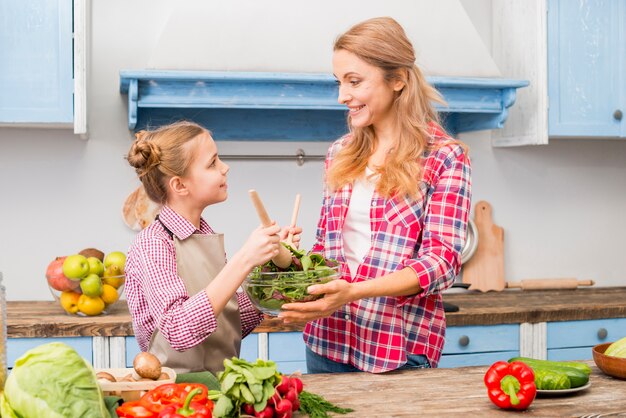 Vista laterale di una figlia che aiuta sua madre a preparare insalata