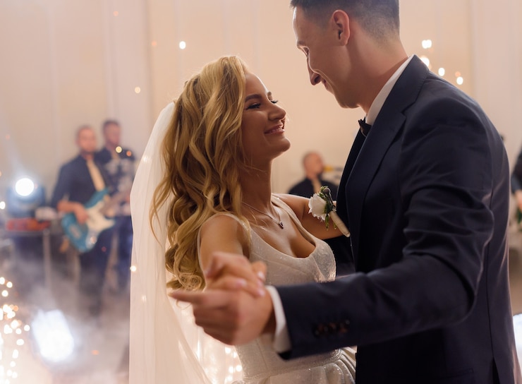 Foto gratuito vista laterale di una giovane coppia sposata sorridente, che celebra il proprio matrimonio, si tiene per mano e balla
