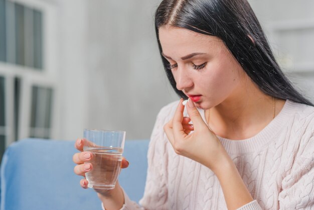 Vista laterale di una giovane donna che tiene bicchiere d&#39;acqua che prende medicina