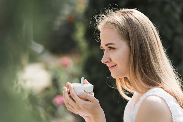 Vista laterale di una giovane donna che tiene tazza di caffè in due mani