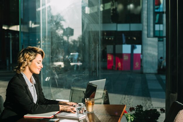 Vista laterale di una giovane donna di affari sorridente che lavora al computer portatile nel ristorante