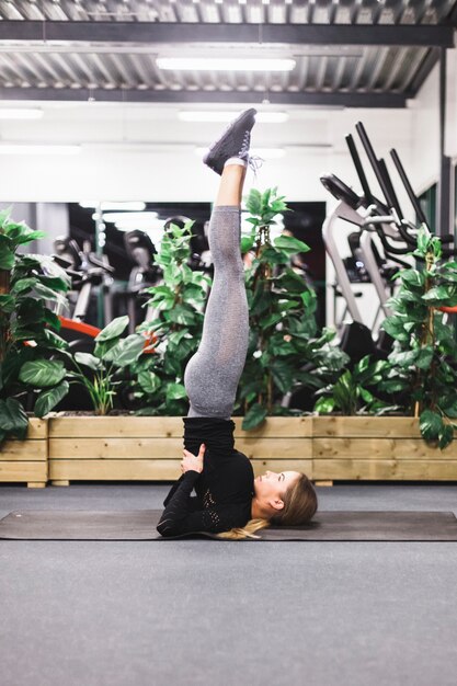 Vista laterale di una giovane donna facendo esercizio di gamba su stuoia di yoga