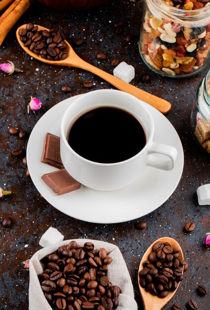 Vista laterale di una tazza di caffè con cioccolato e un cucchiaio di legno con chicchi di caffè su sfondo nero