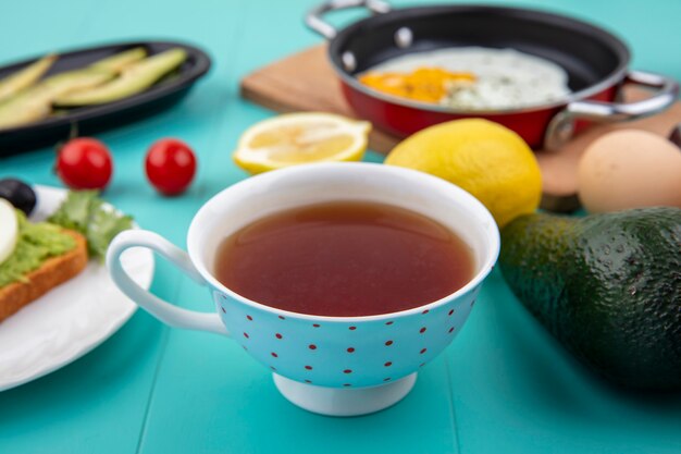 Vista laterale di una tazza di tè con l'uovo fritto del limone su una pentola su un bordo di legno della cucina con gli ingredienti sulla superficie del blu