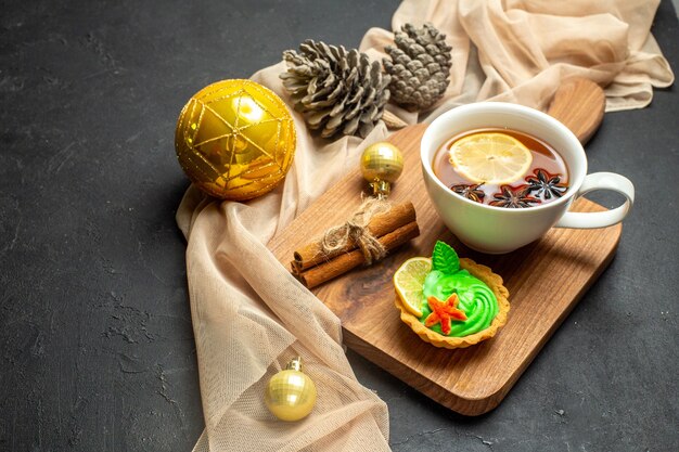 Vista laterale di una tazza di tè nero con accessori per la decorazione del nuovo anno al limone e cannella sul tagliere di legno