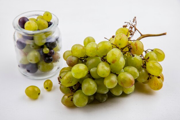 Vista laterale di uva bianca e bacche di uva in vaso su sfondo bianco